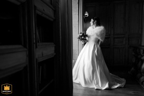 Black and white profile shot of a winter bride standing by a doorway, waiting for her groom at Chateau des Girards, France.